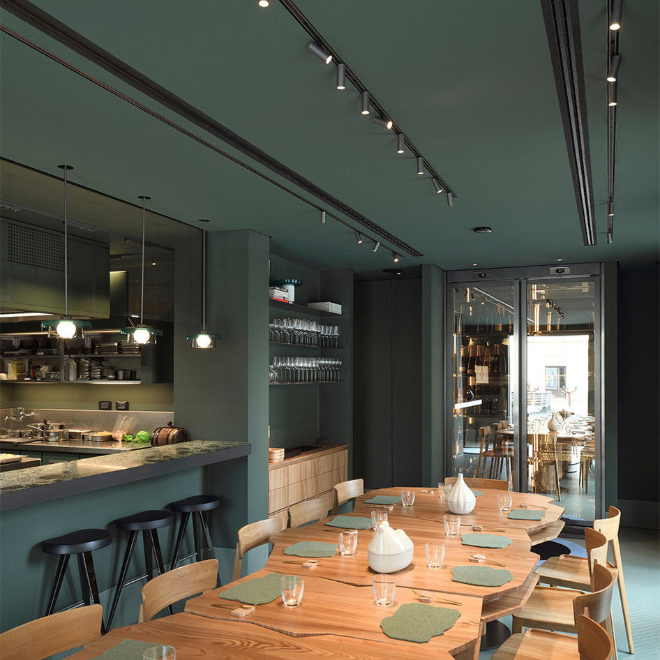 Interior of Davide Oldani’s Olmo restaurant featuring a green ceiling, black tracks with Artemide’s Turn Around fixtures, wooden furniture and a refined table setting.