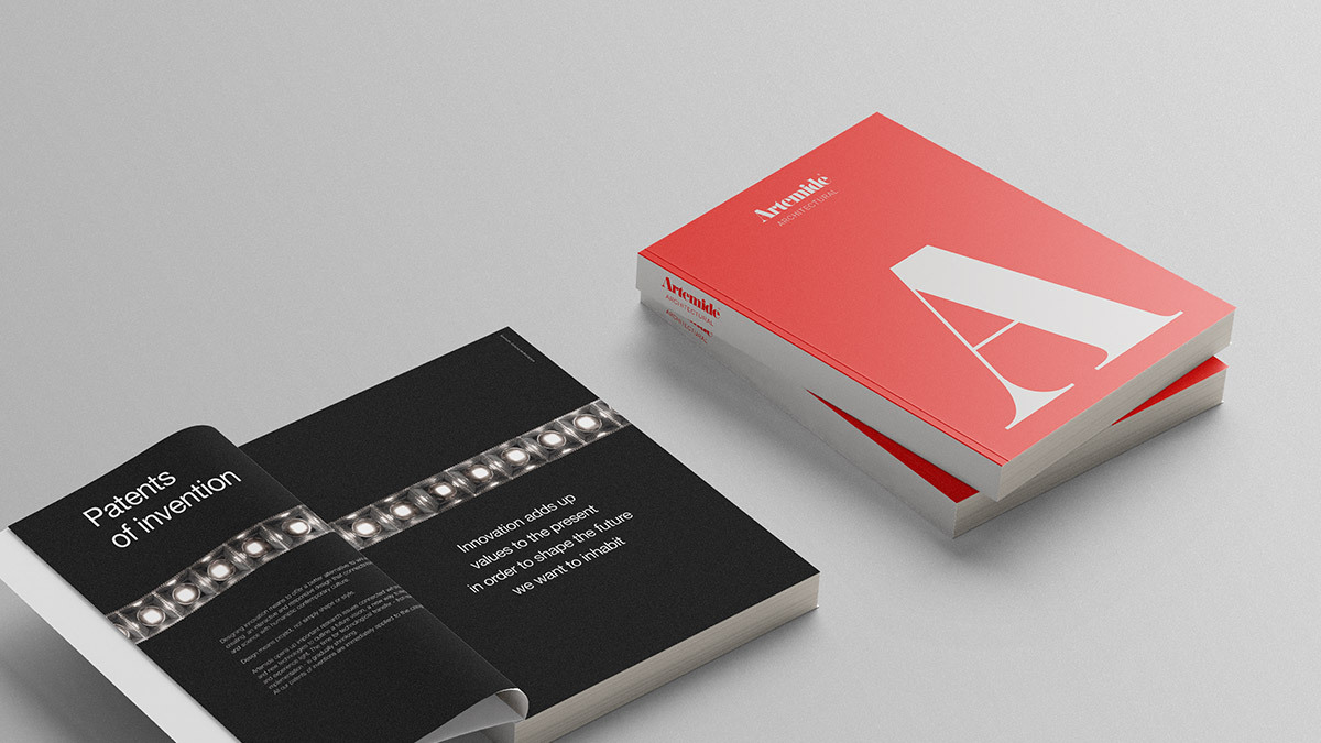 Top view of the Artemide Architectural 2025 catalogue, with one closed copy featuring a red cover and large white letter A, and one open copy showing a black double-page spread about patents and innovation.