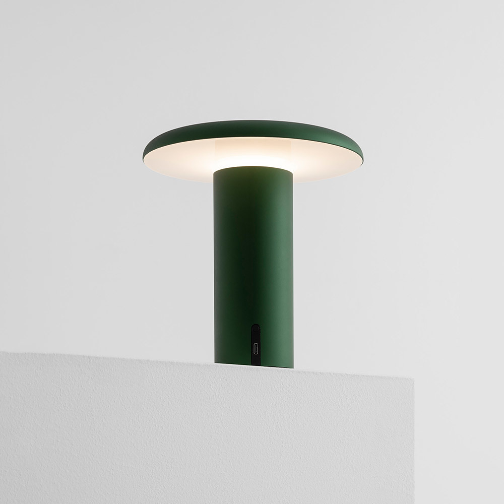 Portable Takku table lamp made of green anodized aluminium with luminous disc diffuser and cylindrical body.