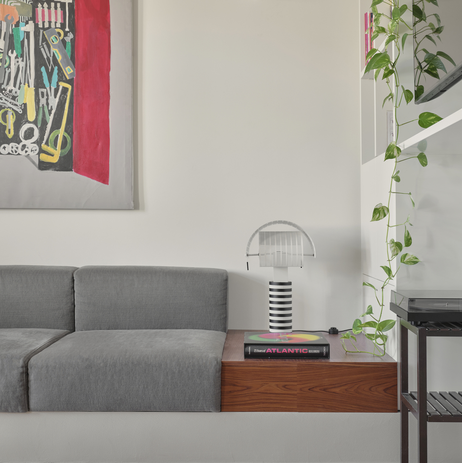 Artemide’s Shogun table lamp on a wooden surface in the living area, beside a grey sofa and a white bookshelf.