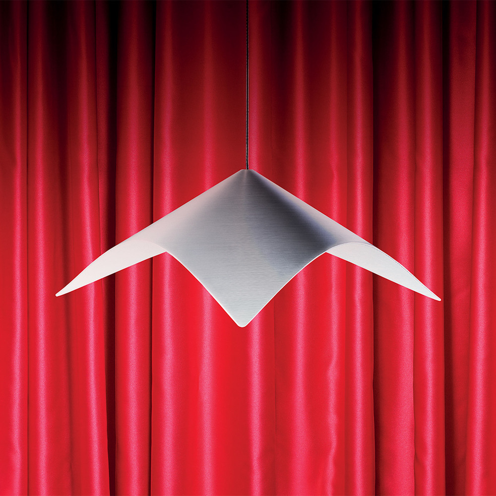 Iperbole pendant lamp in satin-finished metal, with a geometric form, suspended in front of a red curtain. Photo by Pierpaolo Ferrari.