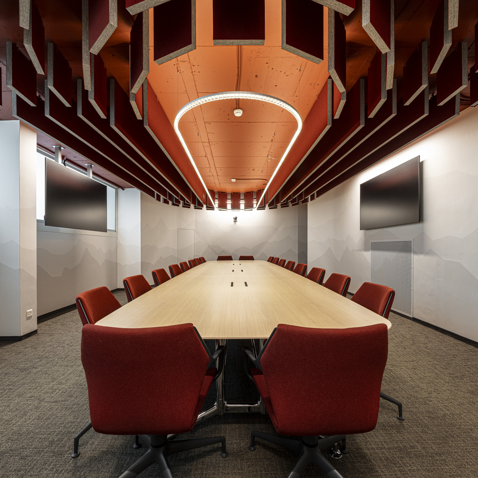 Meeting room with a large central table, red chairs and the Somnĭum lighting system installed on the ceiling.
