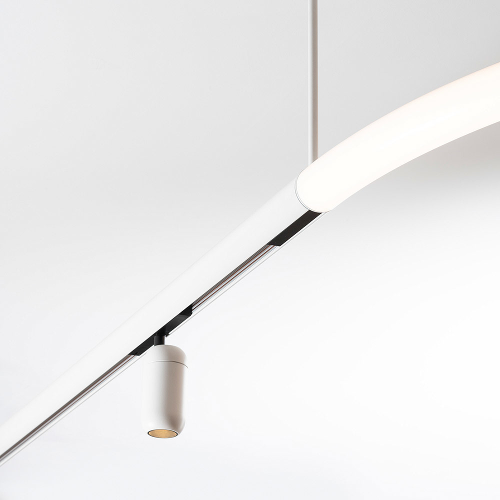 Système d'éclairage sur rail blanc avec un spot cylindrique suspendu et une barre LED linéaire courbée fixée au plafond