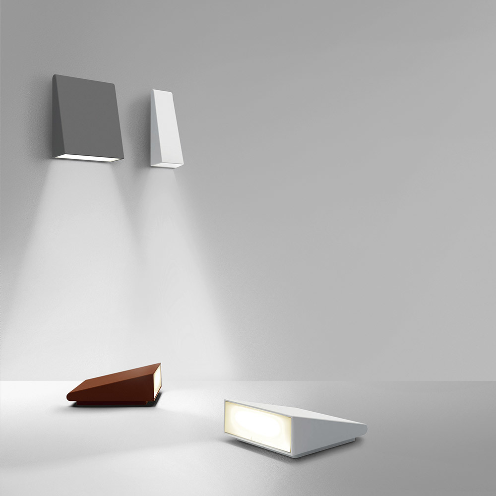 Deux appliques murales grise et blanche émettent des faisceaux lumineux vers le bas ; deux lampes de table triangulaires en rouille et blanc reposent sur une surface.