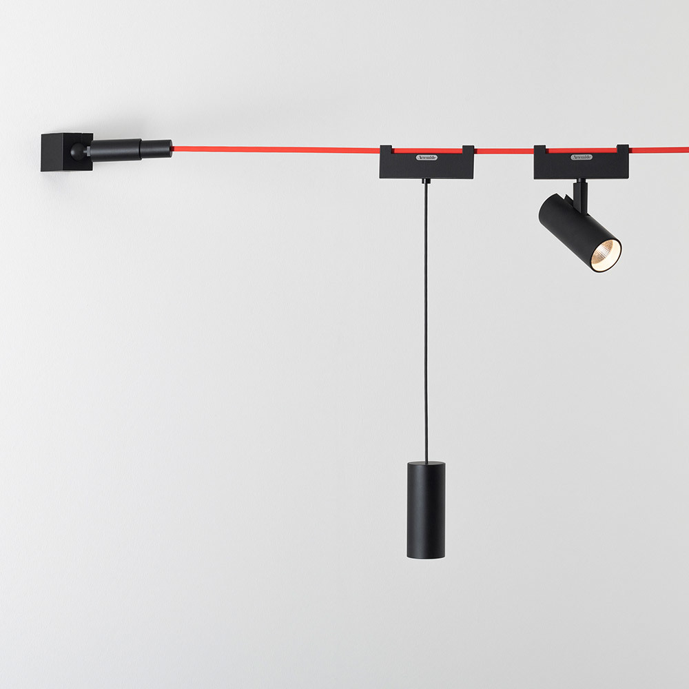 Système d'éclairage sur rail modulaire noir avec câble rouge, comprenant une suspension cylindrique et un spot orientable fixé au mur