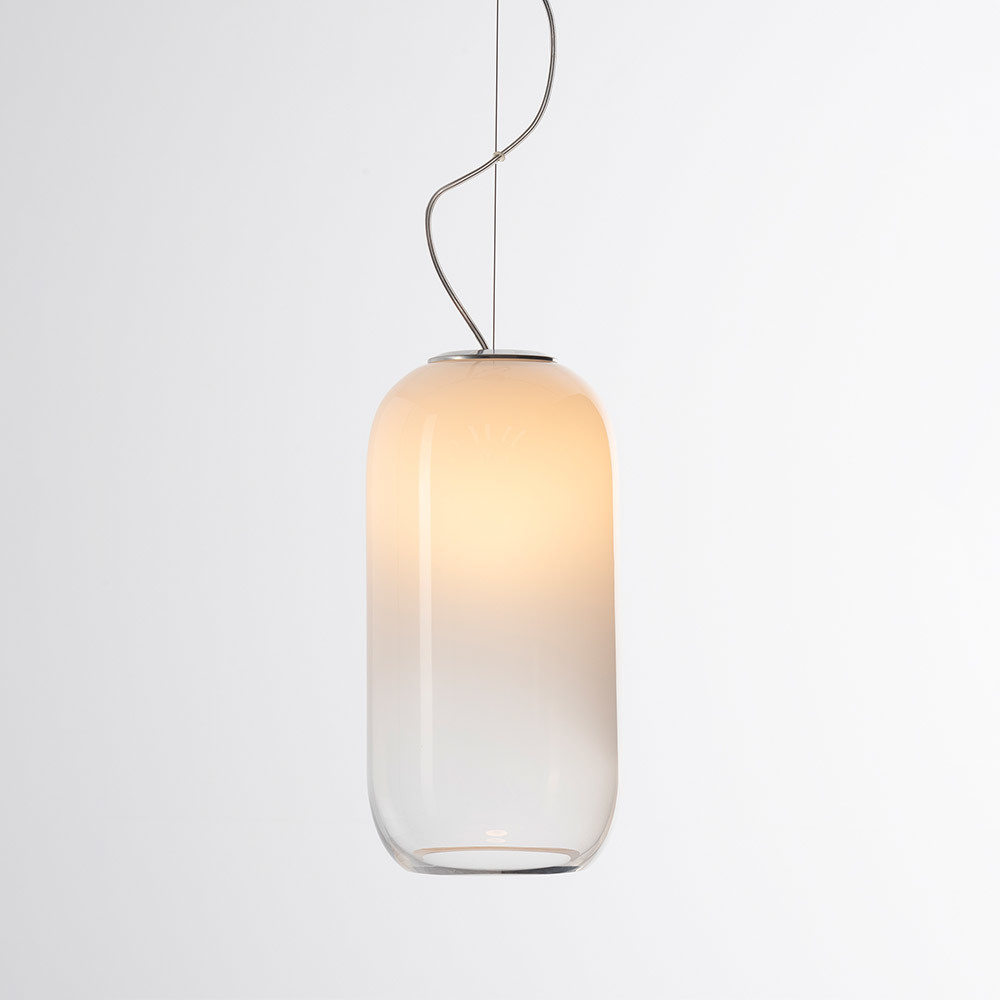 Suspension Artemide avec abat-jour en verre soufflé en forme de capsule allongée, dégradé du blanc chaud en haut au transparent en bas, sur câble argenté