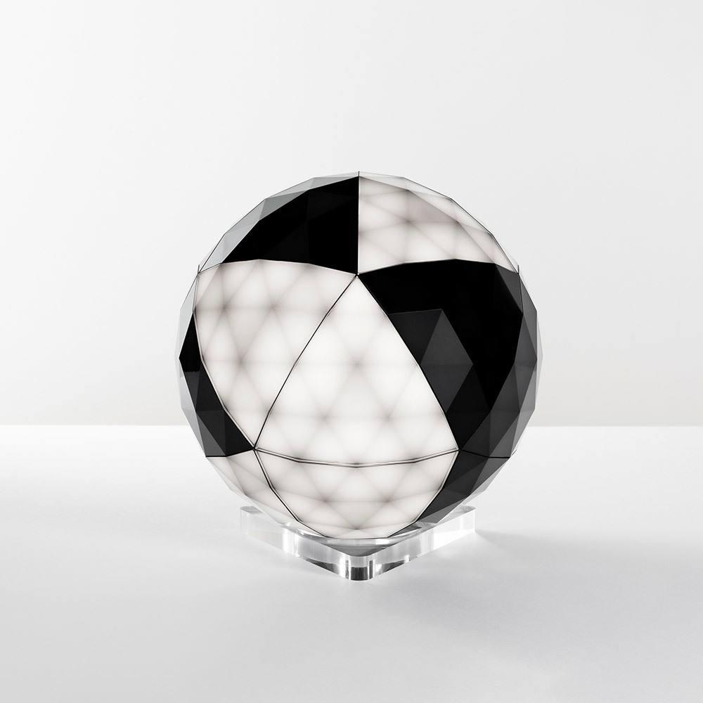 Lampe de table sphérique à surface géométrique facettée, panneaux alternés noirs et blancs, lumière douce diffuse, sur socle en acrylique transparent