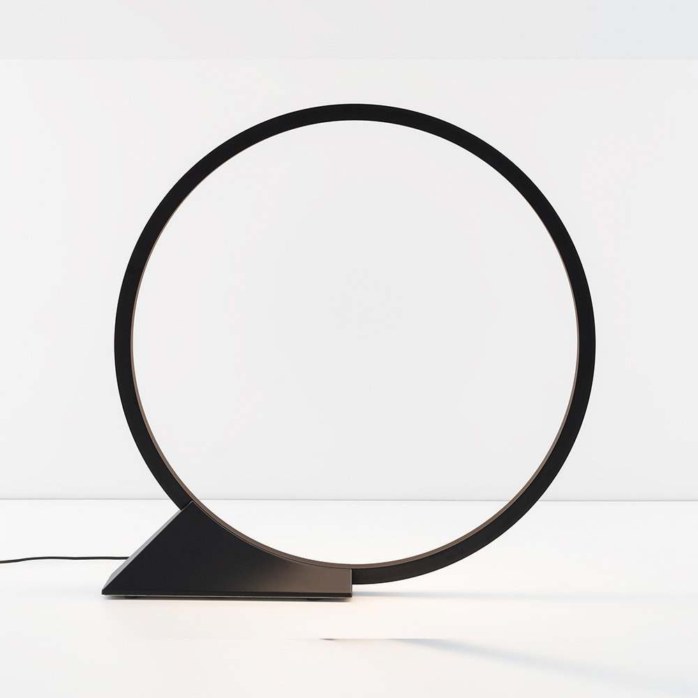 Lampe de table LED noire avec grand diffuseur circulaire en anneau monté sur une base triangulaire, design minimaliste.