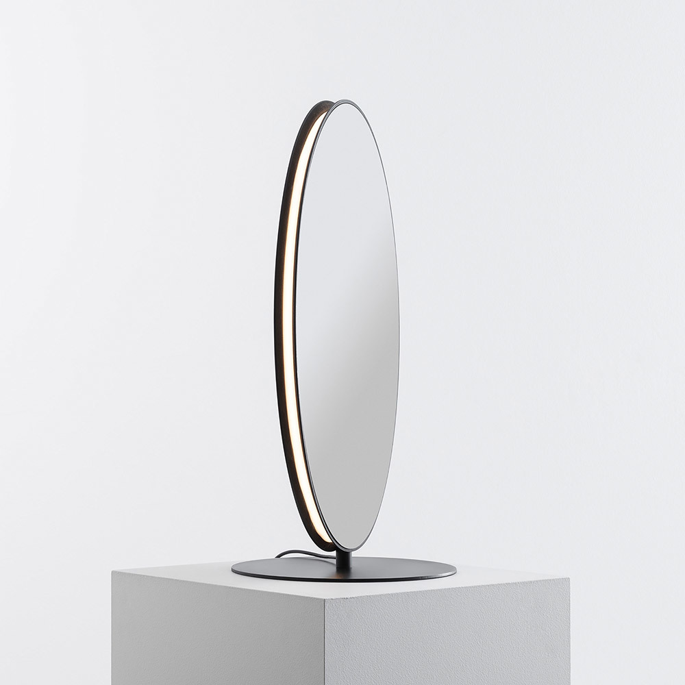 Lampe de table ovale avec cadre en métal noir intégrant un bandeau LED, montée sur une base ronde noire, présentée sur un socle blanc