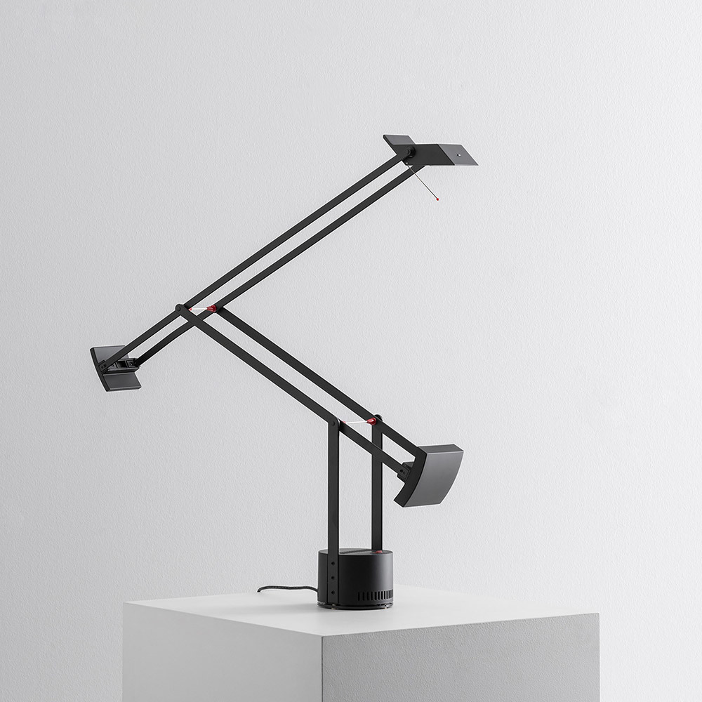 Lampe de bureau Artemide Tizio noire avec double bras à contrepoids, tête orientable et base cylindrique sur surface blanche