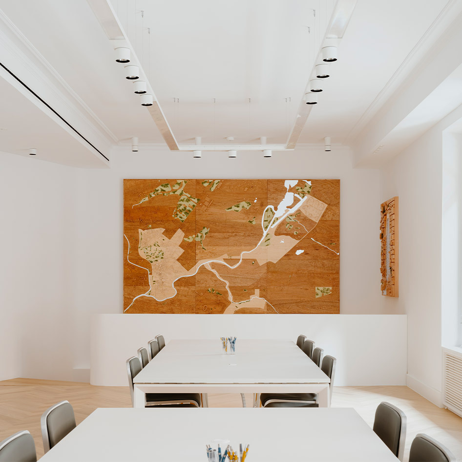 Salle de réunion lumineuse avec tables blanches, chaises grises, œuvre en bois au mur et spots encastrés Artemide au plafond blanc
