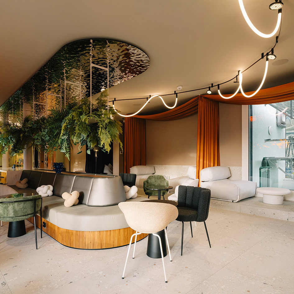 Salon moderne avec rail LED Artemide et suspensions sinueuses style néon, sièges courbés, verdure luxuriante et rideaux orange chaleureux.