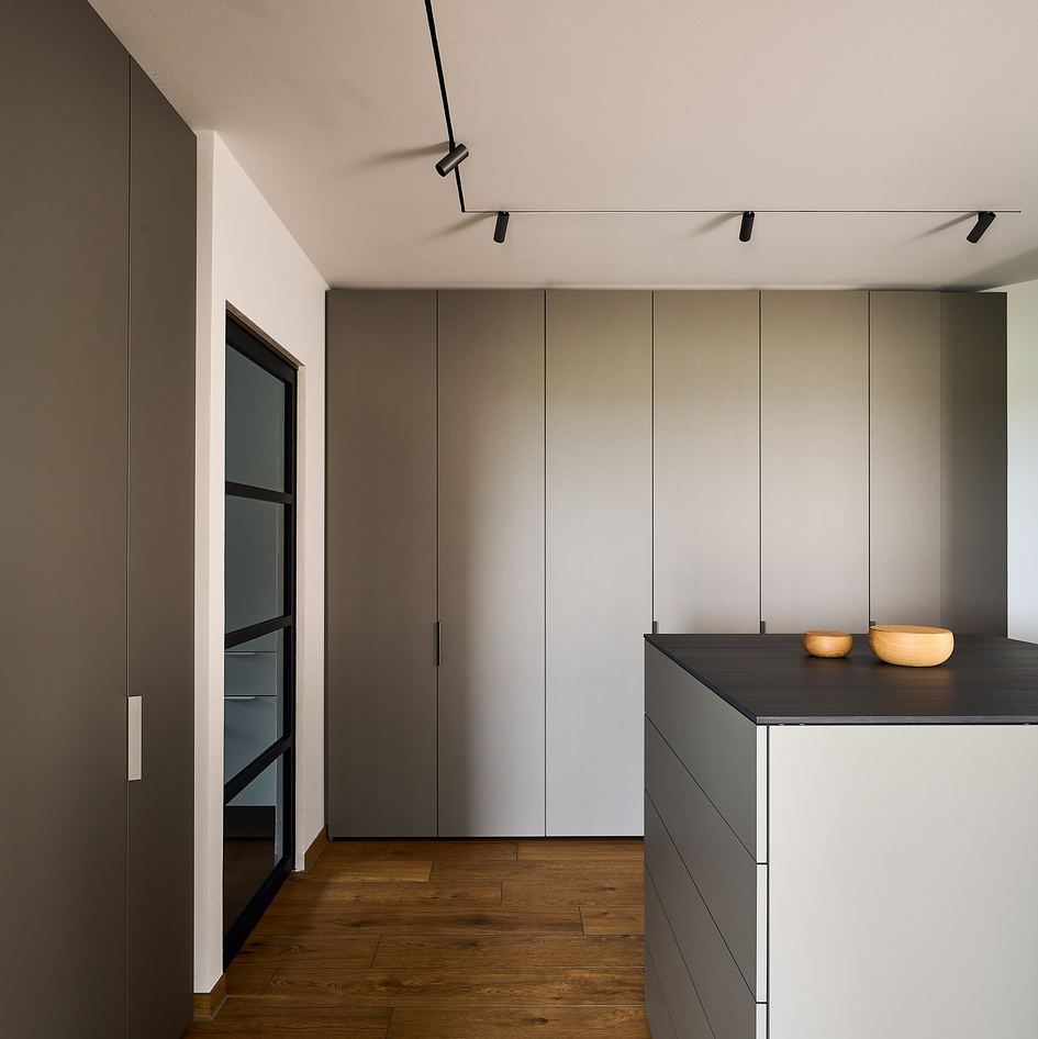 Cuisine moderne avec système de rail Artemide au plafond blanc, spots noirs orientables au-dessus de meubles gris minimalistes et îlot sombre