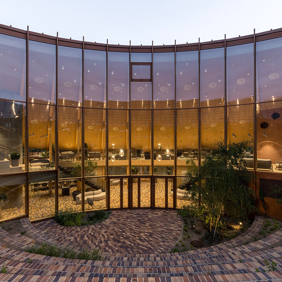 Façade vitrée courbée d'un espace intérieur élégant au crépuscule, avec un éclairage chaleureux, des suspensions et des espaces lounge à l'intérieur.