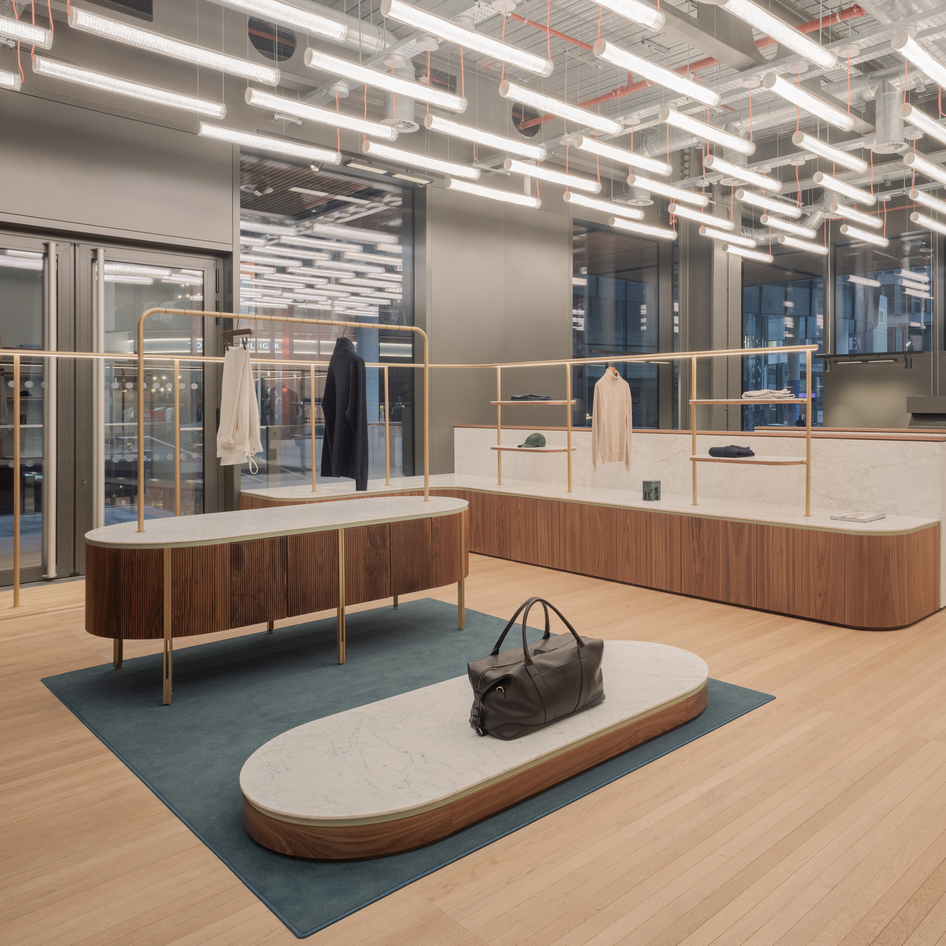 Intérieur commercial moderne avec luminaires linéaires LED Artemide au plafond éclairant des comptoirs en noyer, des portants en laiton et un parquet clair.