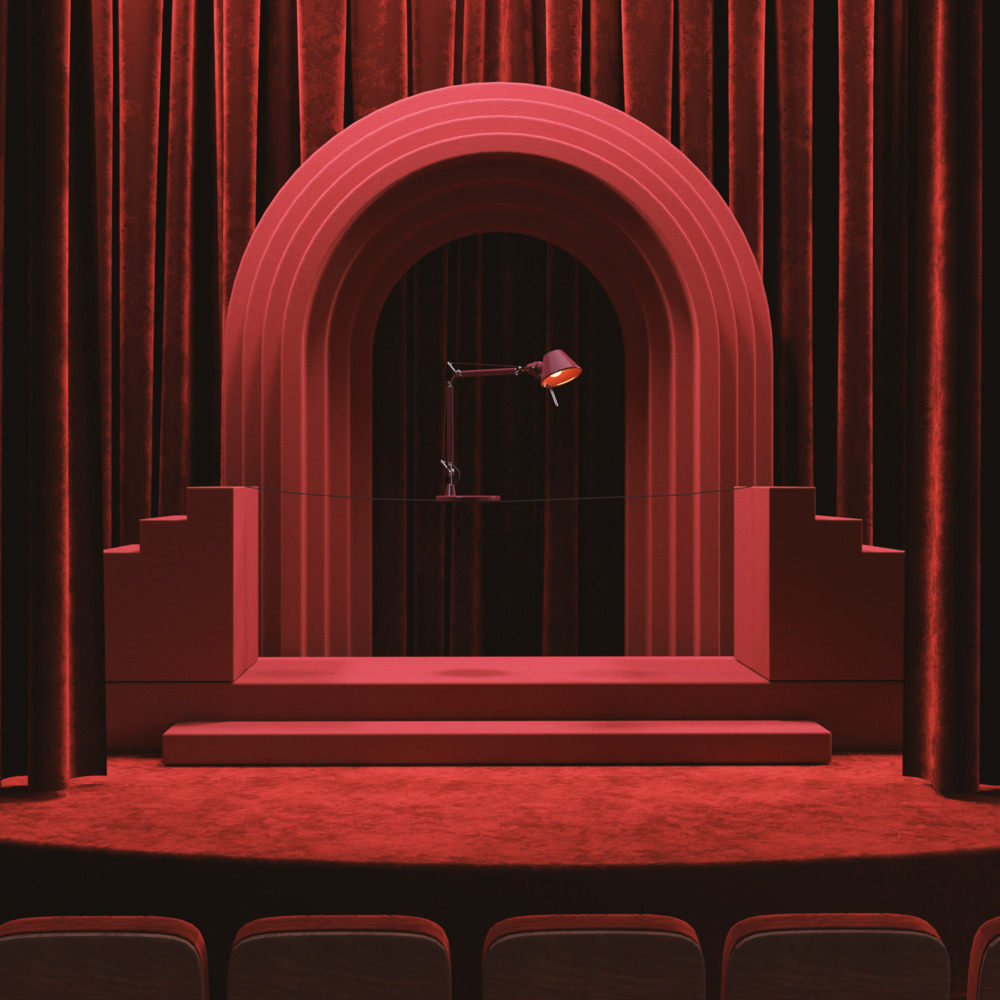 Lampe de bureau Artemide sur une scène théâtrale rouge avec arche et rideaux de velours, décor monochrome dramatique en rouge
