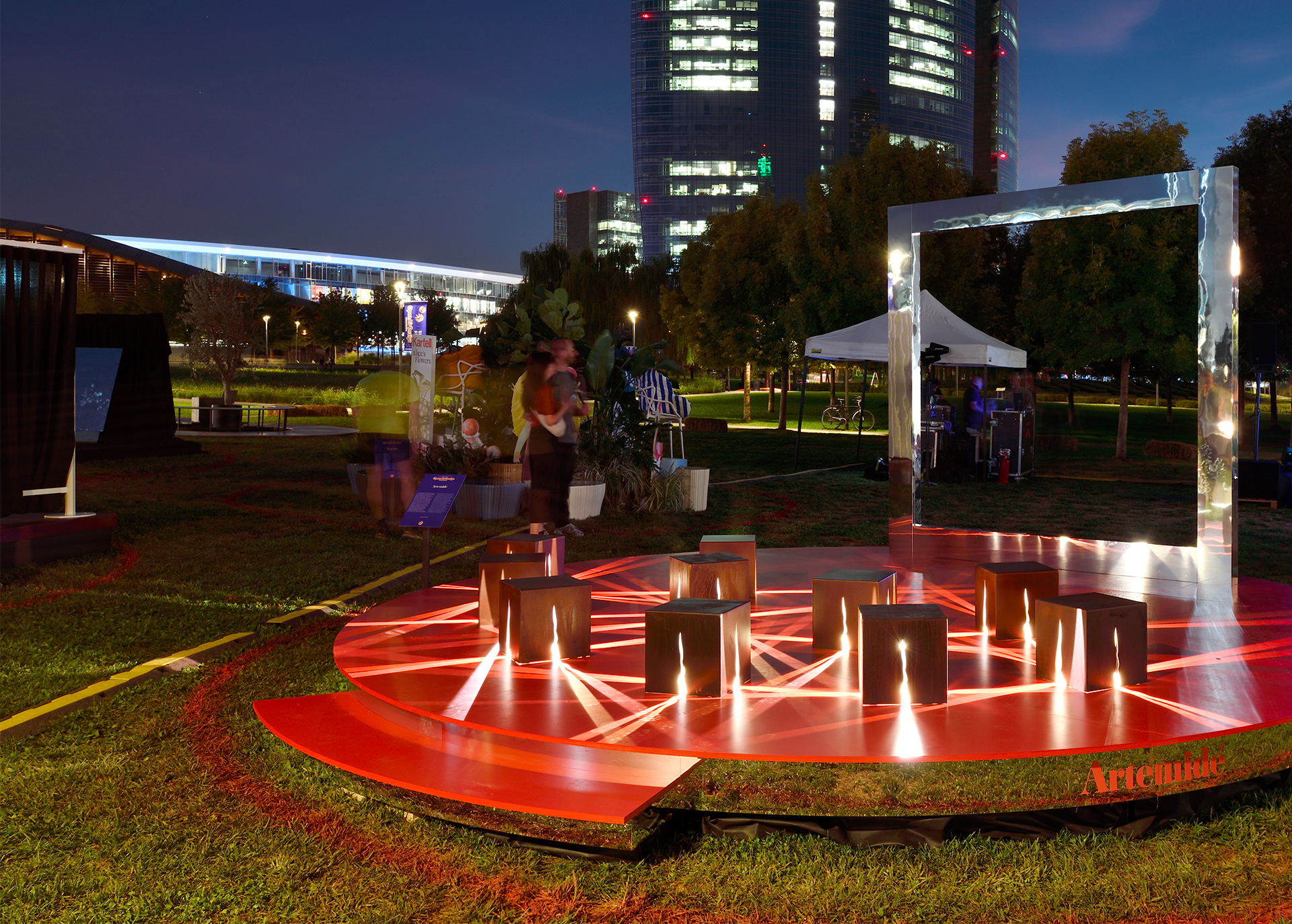 Light installation with cubes and red beams in an urban park at night.