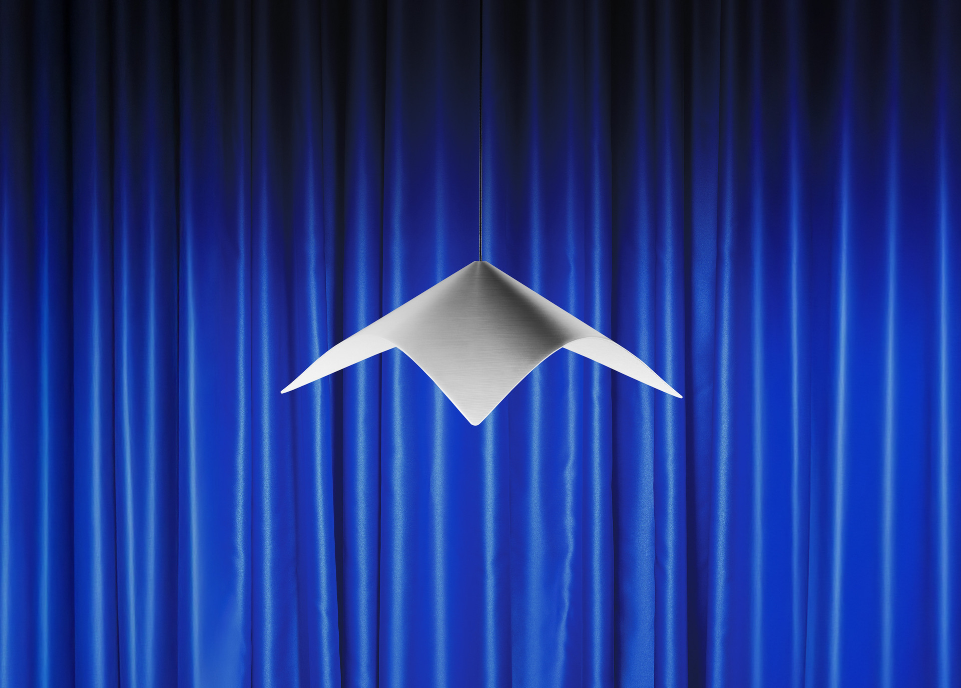 Iperbole pendant lamp in front of blue theater curtains.