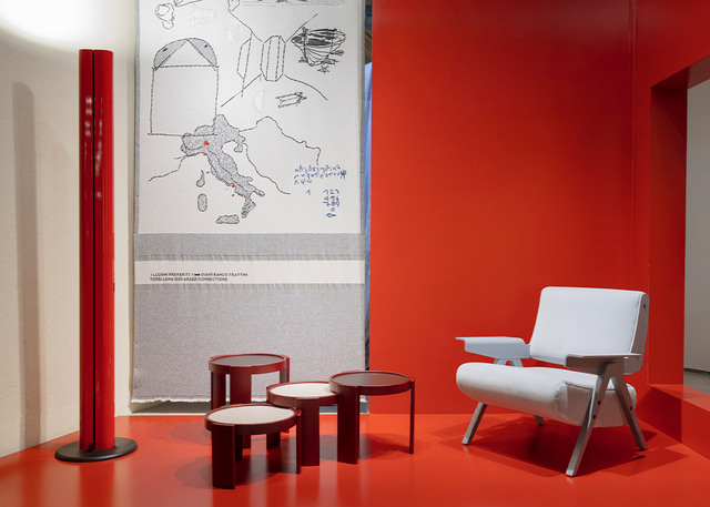 Exhibition display for the 100th anniversary of Gianfranco Frattini, featuring the red Megaron lamp, side tables, and a design armchair against a red backdrop.