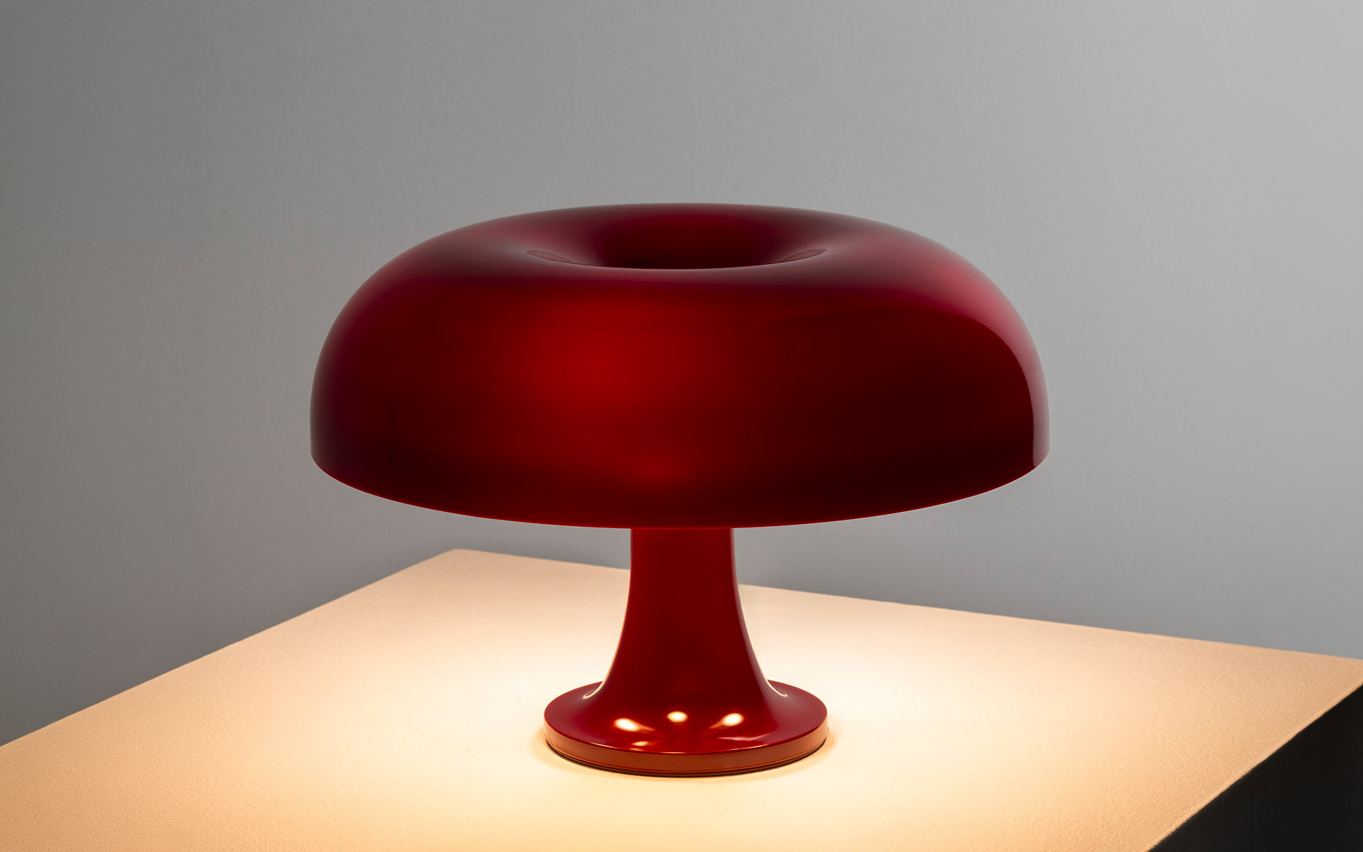 Lit bordeaux Nessino lamp on a white plinth.