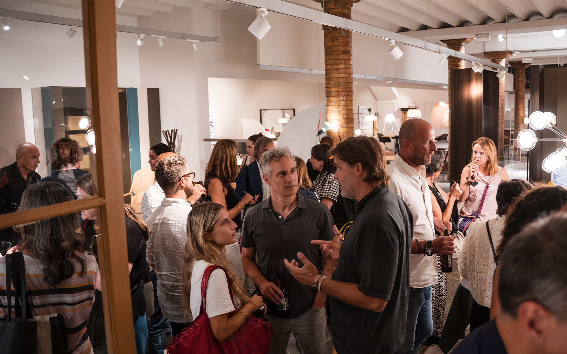 Guests mingling at an Artemide lighting showroom event, with various lamps and fixtures displayed on walls and ceiling.