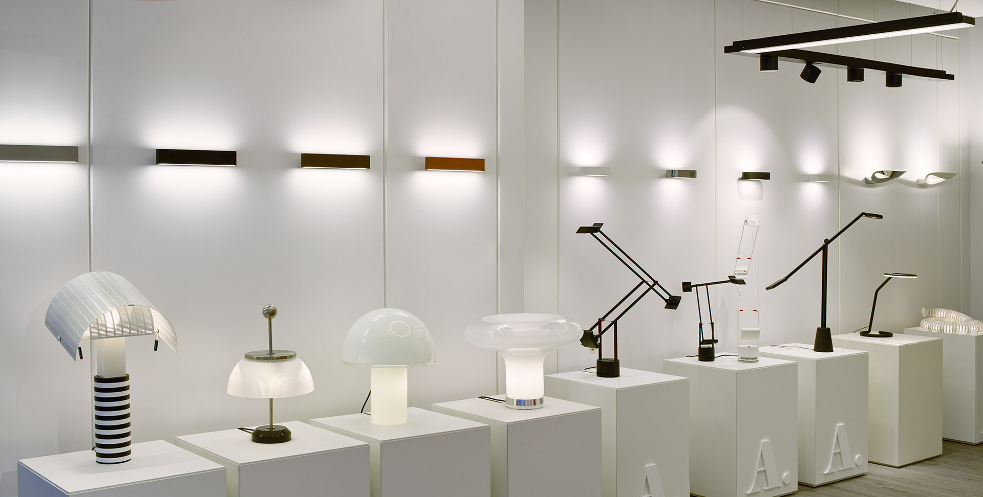 Showroom Artemide con lampade da tavolo, applique e lampade da lavoro su piedistalli bianchi, immersi in una calda luce d'ambiente