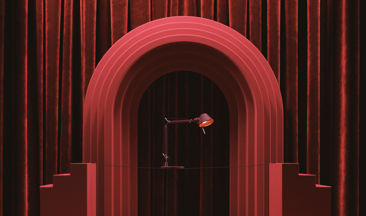 Bordeaux Tolomeo Micro table lamp displayed on a stage with a scenic arch and velvet curtains.