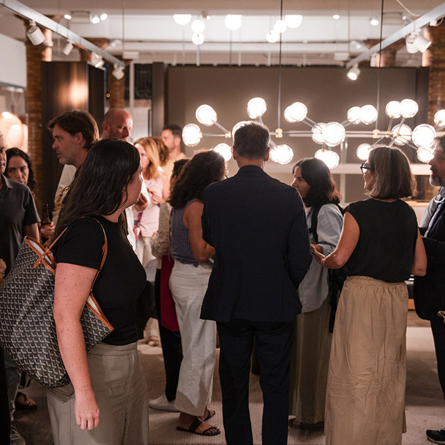 Guests mingling at an Artemide showroom event, with a large multi-globe chandelier illuminating the elegant space.