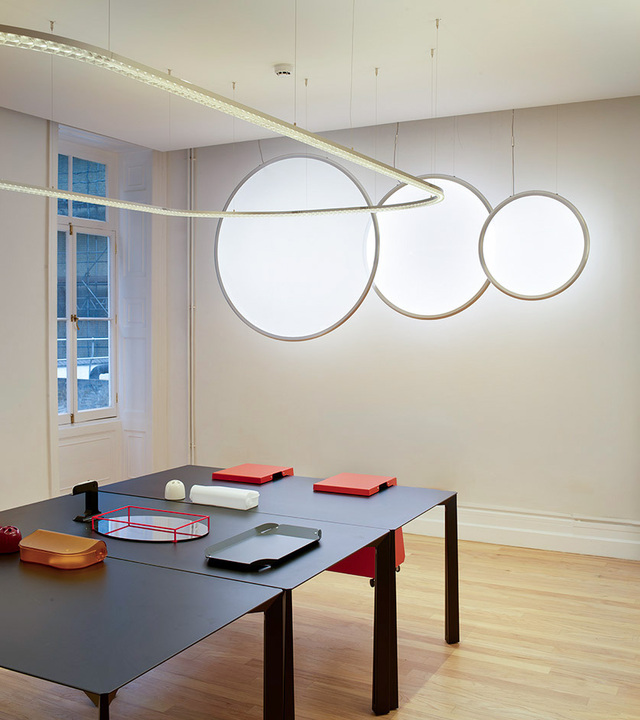 Sistema Somnium e lampade Discovery circolari di Artemide sospesi sopra tavoli scuri in un ambiente contemporaneo.