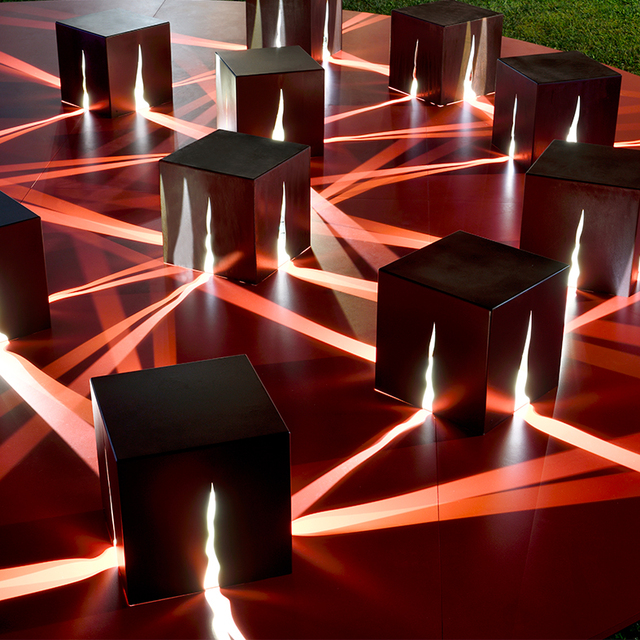 Black luminous cubes on red platform with crossing light beams forming geometric patterns.