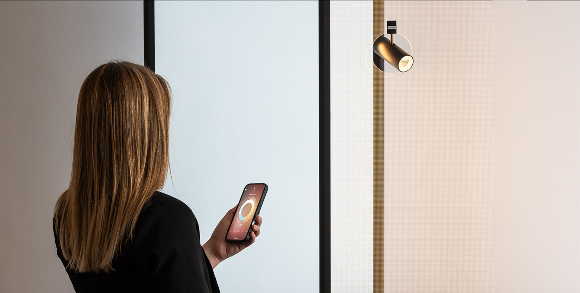 Woman controls a wall spotlight using a smartphone app.