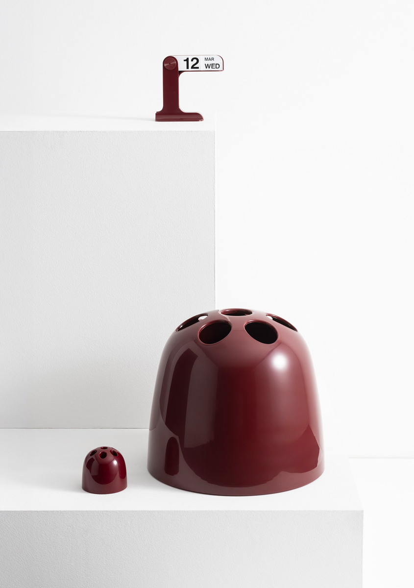 Composition of bordeaux Danese Milano design objects on white plinths.