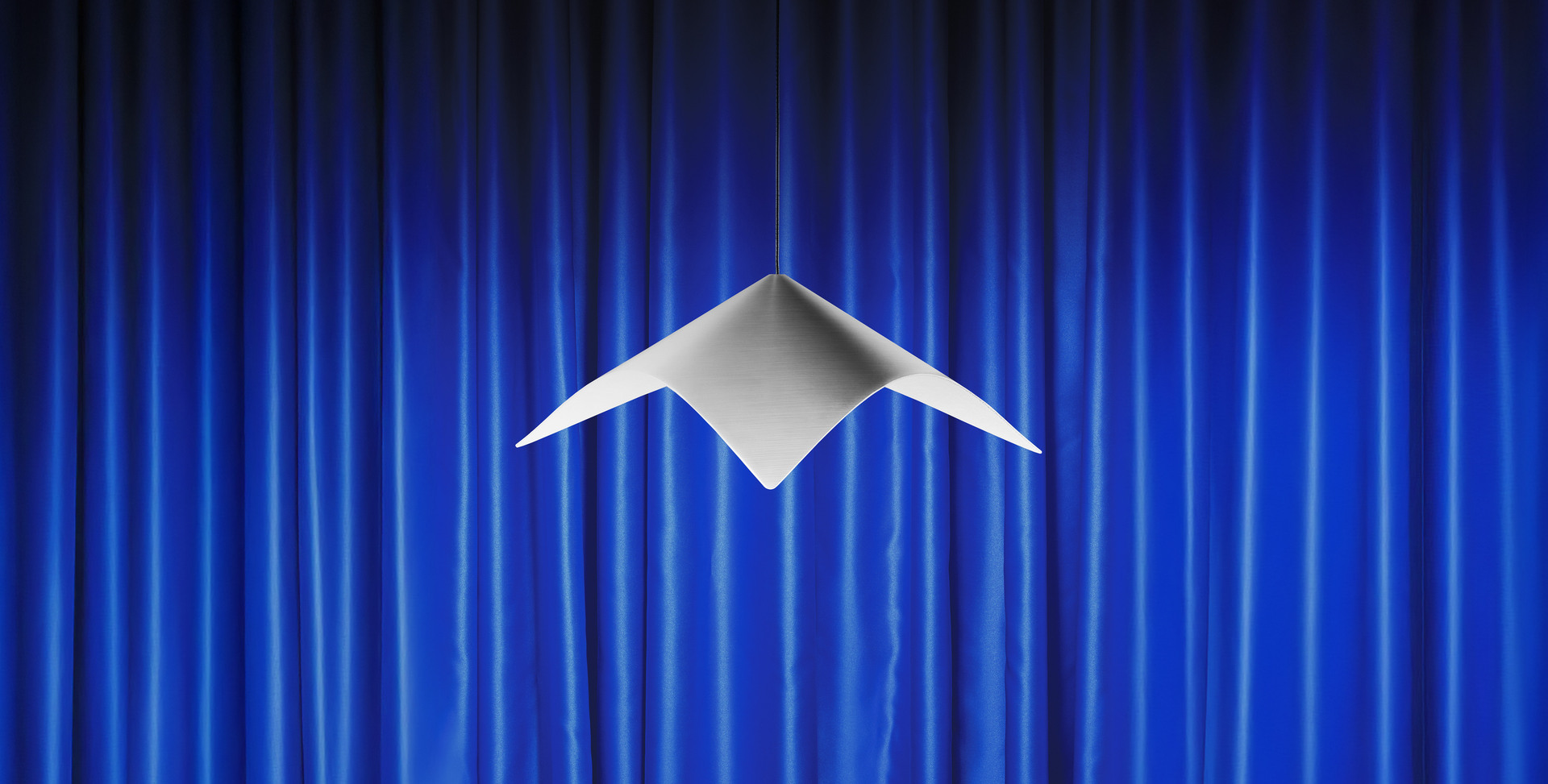 Iperbole pendant lamp in front of blue theater curtains.