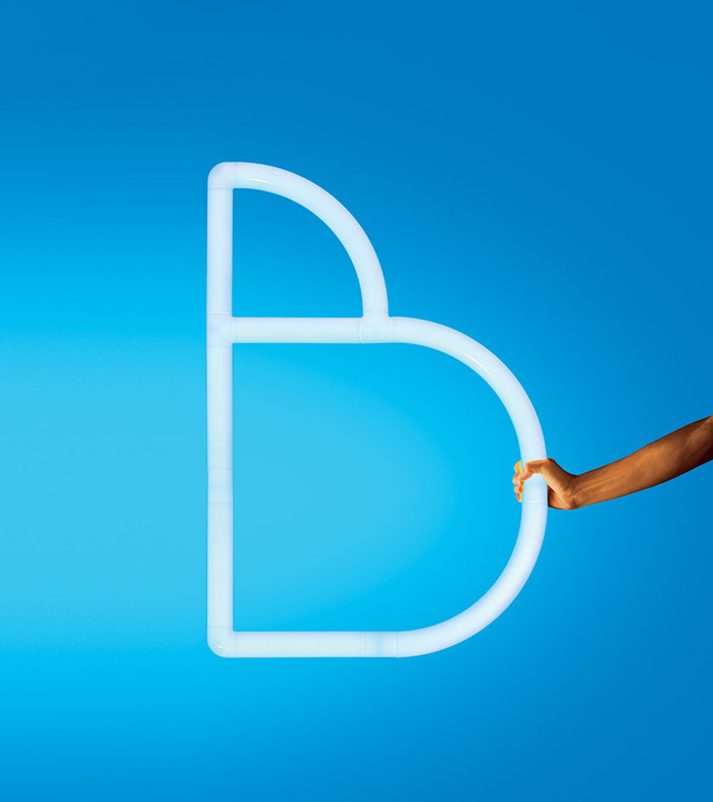 Alphabet of Light luminous letter B against a blue background, held by a hand on the right side. Photo by Pierpaolo Ferrari.