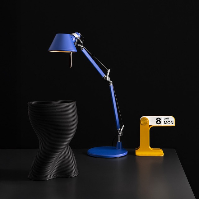 Blue Tolomeo lamp and yellow Timor calendar displayed on a table against a black background.