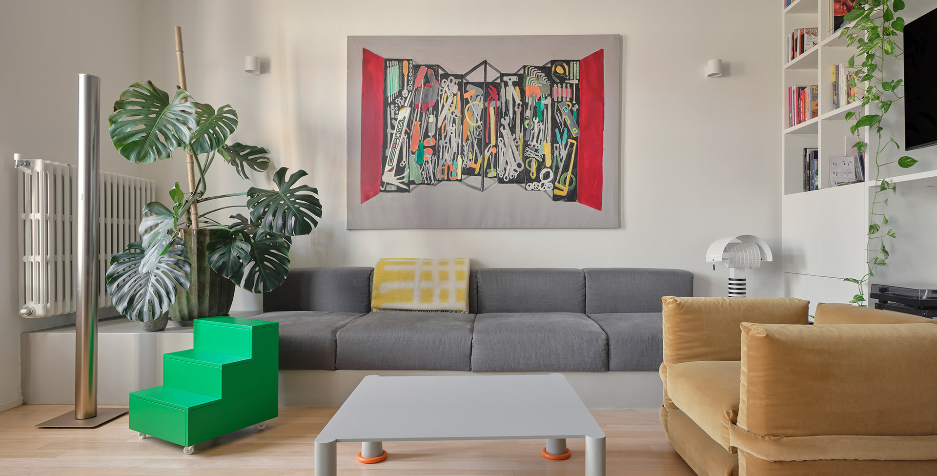 Living room with Artemide’s Ilio 10 and Shogun lamps, a grey sofa, an ochre armchair and a custom white bookshelf.