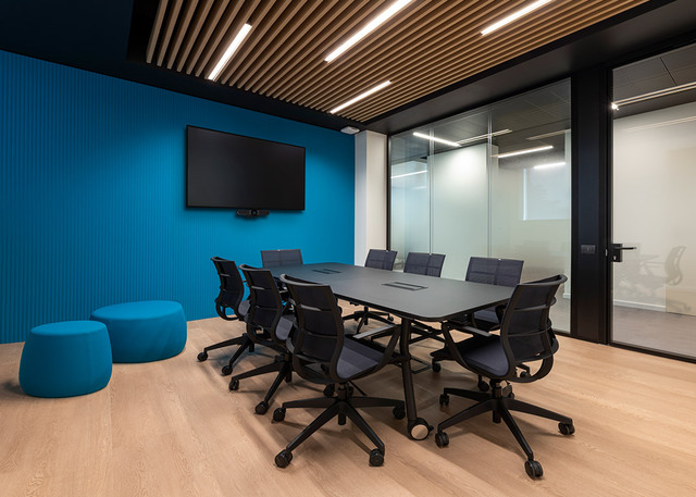Meeting room with blue feature wall, grey conference table, black ergonomic chairs and wooden slatted ceiling with integrated controlled-emission lighting.