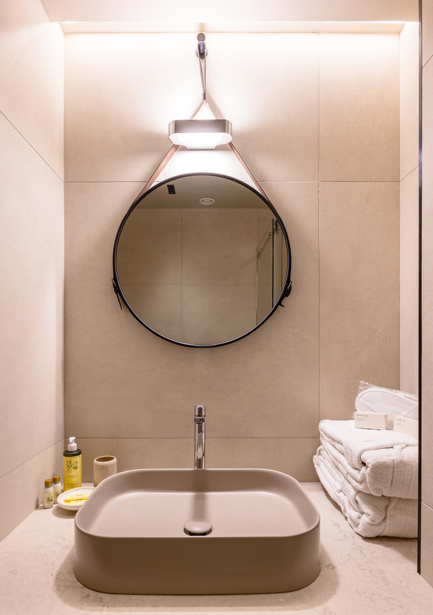 Bathroom vanity with round mirror, vessel sink, and an Artemide wall lamp with leather strap mount providing warm accent lighting.