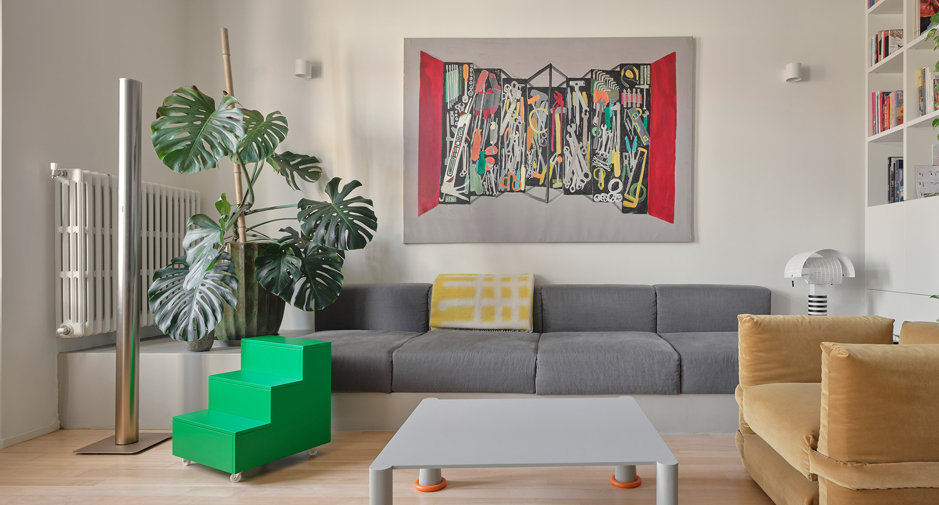 Living room with Artemide’s Ilio 10 and Shogun lamps, a grey sofa, an ochre armchair and a custom white bookshelf.