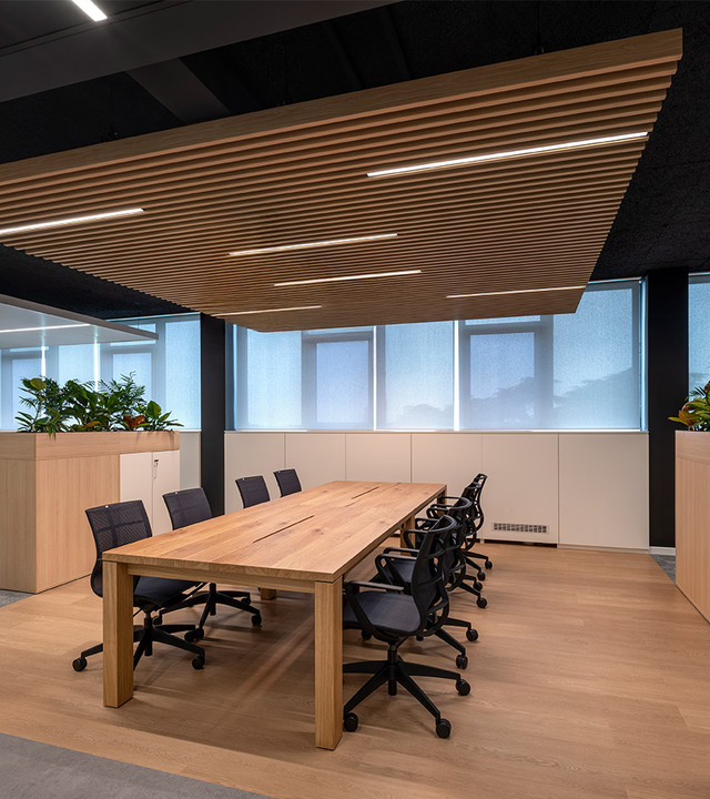 Office with solid wood table, black ergonomic chairs and wooden slatted ceiling with integrated controlled-emission lighting.