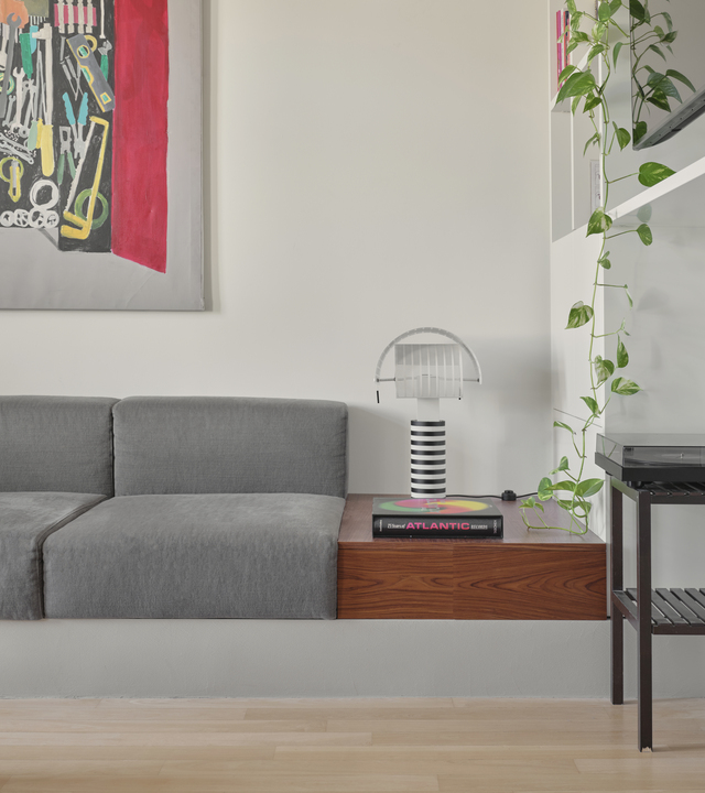 Artemide’s Shogun table lamp on a wooden surface in the living area, beside a grey sofa and a white bookshelf.