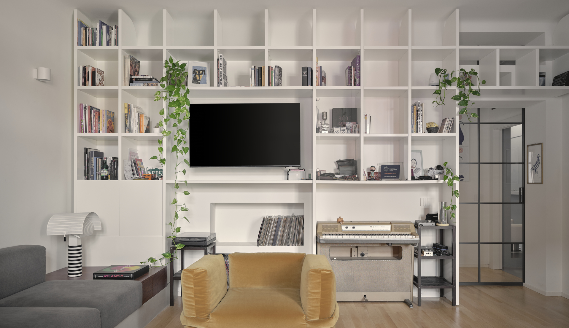 Frontal view of the living area with wall shelving, an ochre velvet armchair and Artemide’s Shogun lamp.