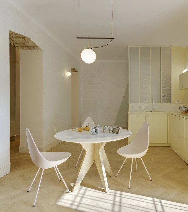 Dining area with a round table, white chairs, and a pendant lamp in a light-toned, minimalist interior.