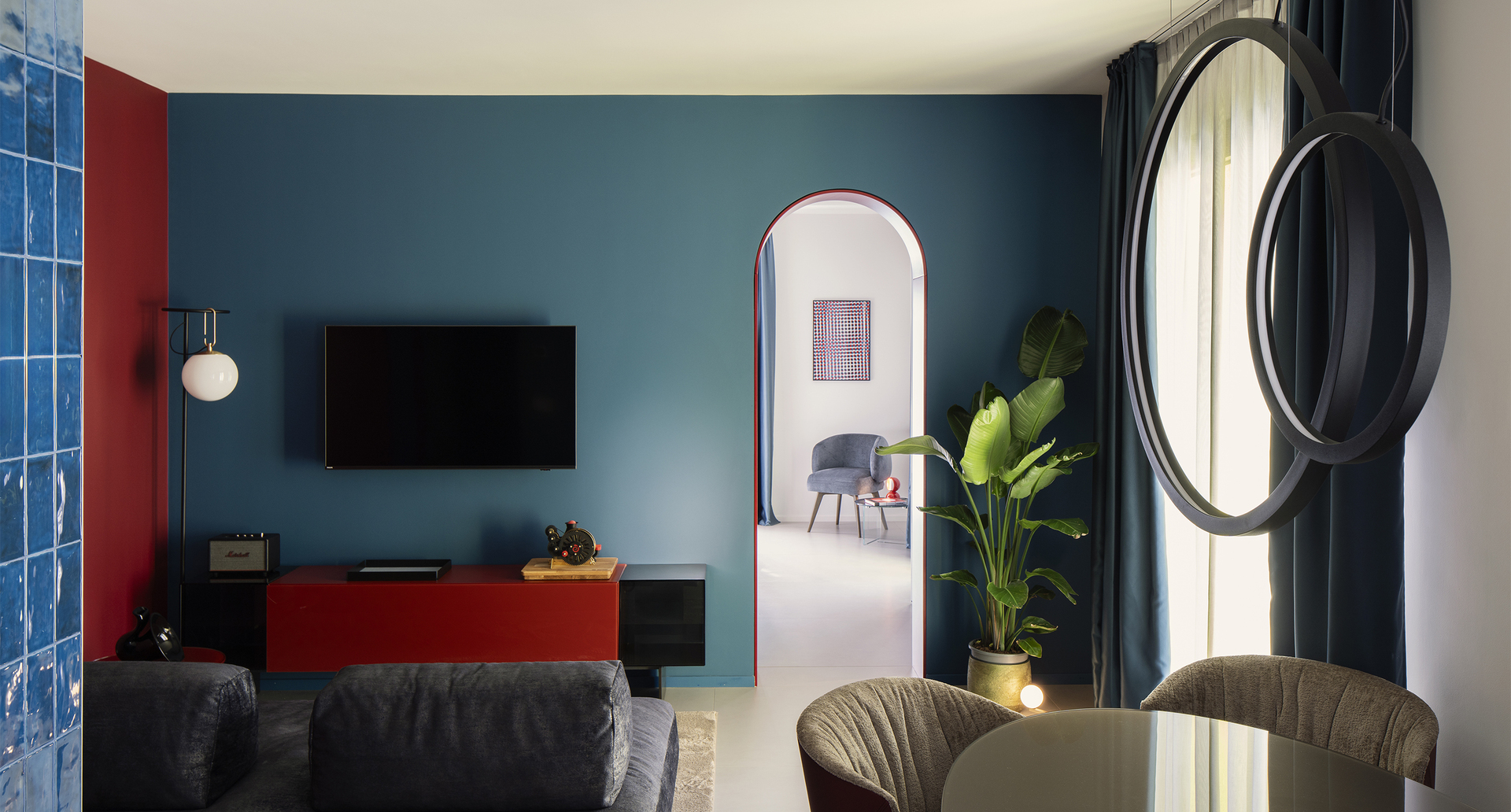 Inside the suite: a cozy living room with a table illuminated by “O” suspension lights, an elegant sofa, and an nh floor lamp near the TV cabinet.