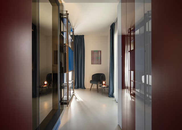 View of the corridor leading to the bedroom, with a chair and a small table featuring an Eclisse lamp at the end.