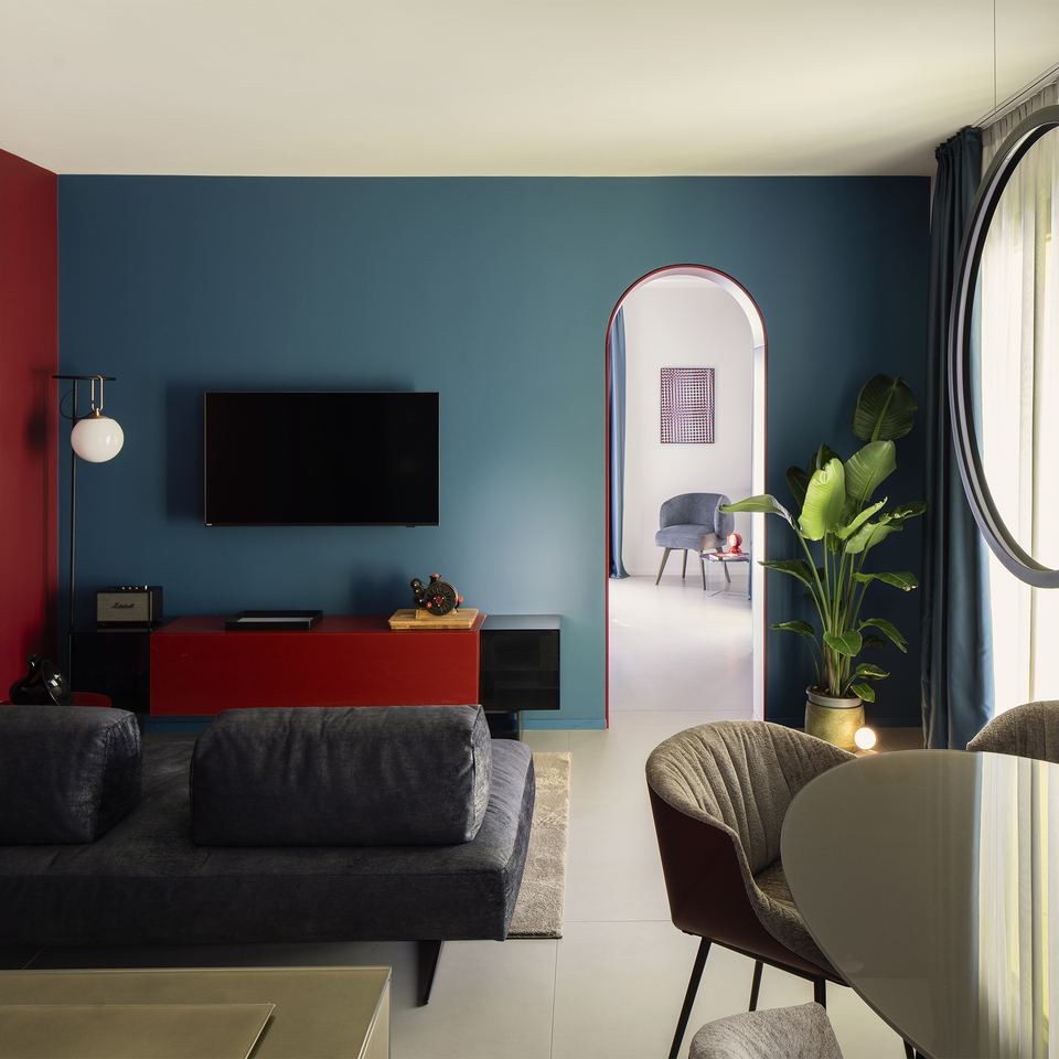 Inside the suite: a cozy living room with a table illuminated by “O” suspension lights, an elegant sofa, and an nh floor lamp near the TV cabinet.